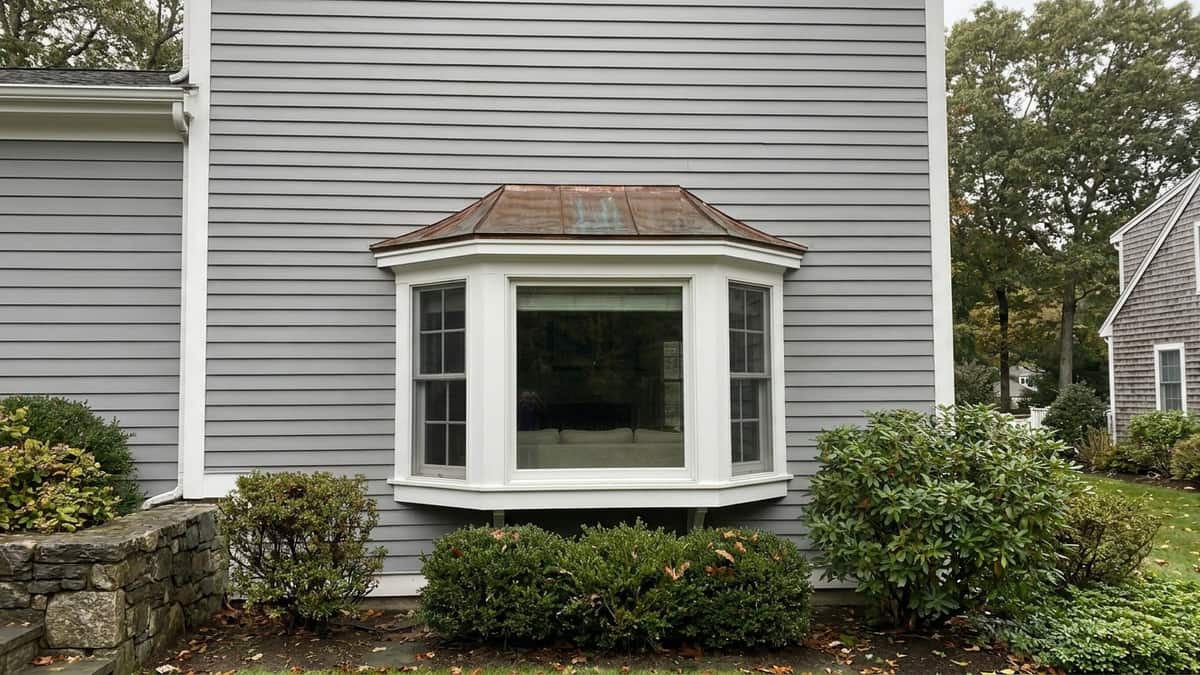 Three-panel bay window projecting from a gray clapboard Connecticut home with white trim and a metal roof cap above the bay