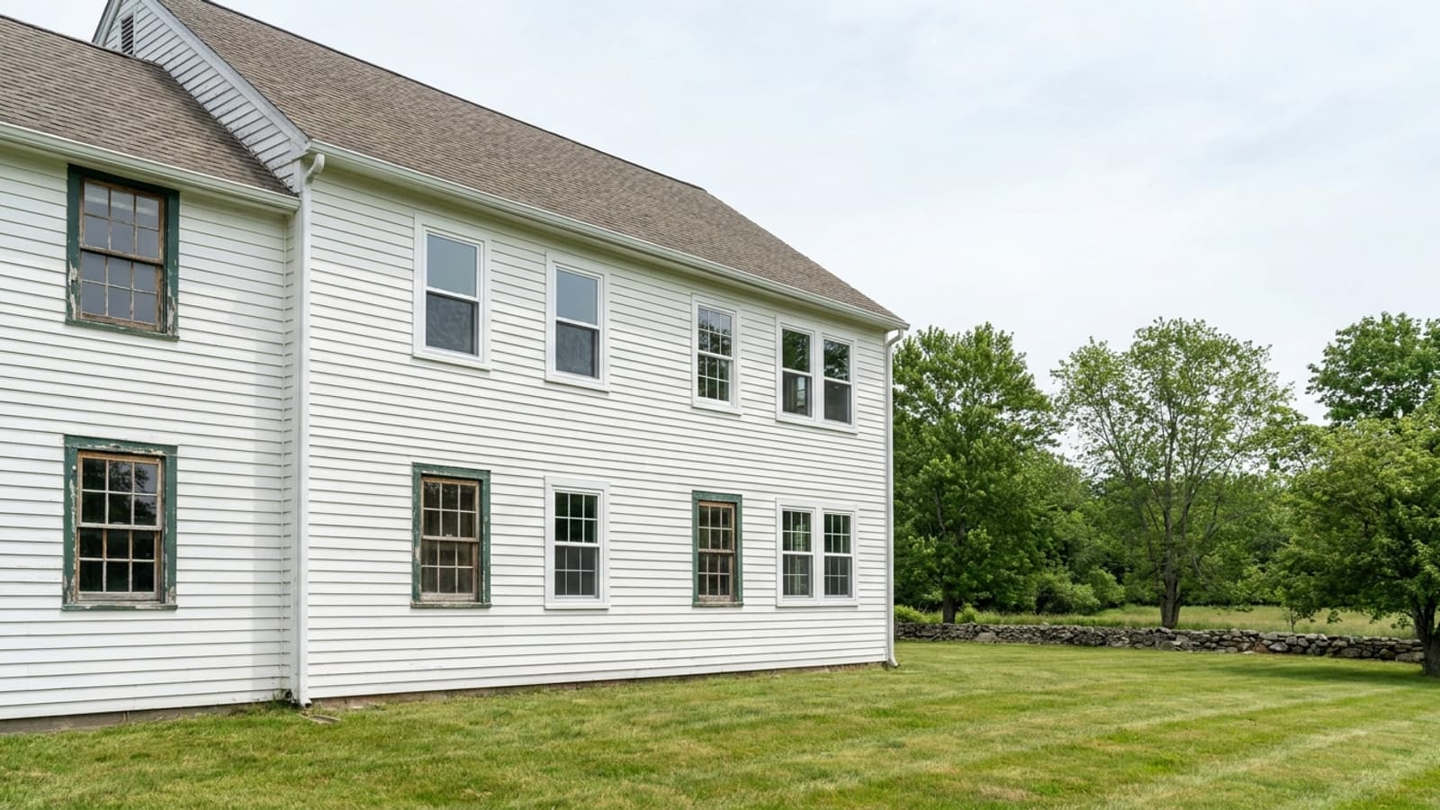 Two-story Connecticut colonial with several crisp new white window frames installed and the remaining windows still showing weathered sashes and peeling trim