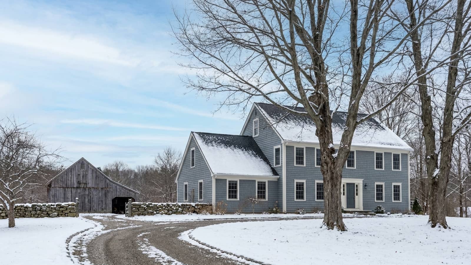 Two-story Connecticut house with a dark asphalt shingle roof lightly dusted in snow, bare maple trees and a snow-edged driveway under a pale blue winter sky